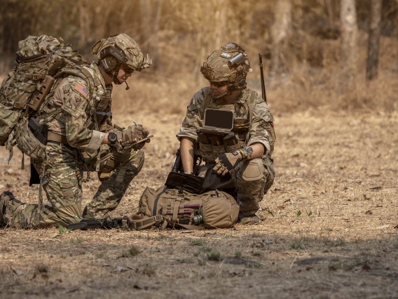 Two Army Soldiers sitting and kneeling on ground in discussion