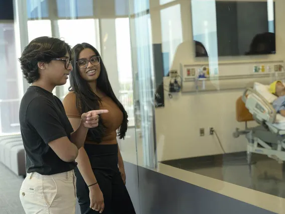 Two female undergrads looking into the medical simulation lab.