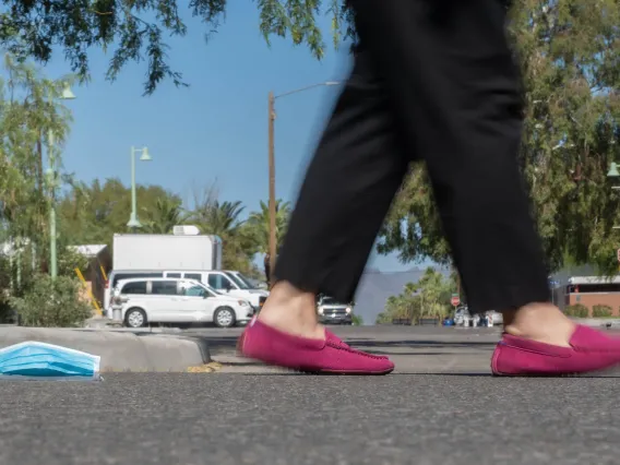 Photo of side walk and person walking by a blue medical mask on the ground