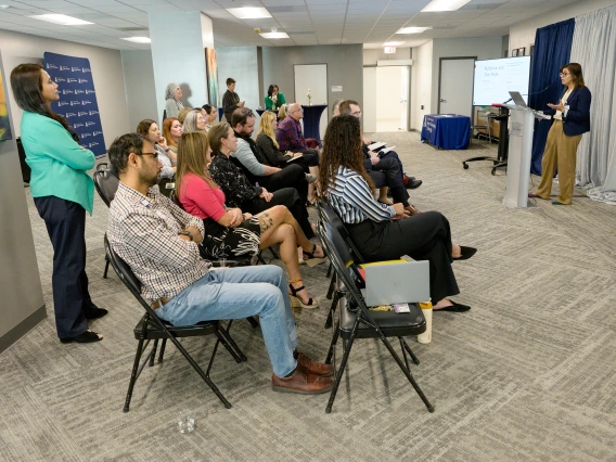 [With her division chief, Mindy Fain, MD, watching near the far pillar, and her husband Talha Riaz, MD, of the Infectious Diseases division, in the foreground, LAMS Fellowship graduate and GGP division internist Saher Khalid, MD, presents on her leadership project May 6, 2025, at the Sparking Change Celebration.]