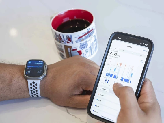 [A cup of coffee next to a man's hands, one wearing a smart watch and the other holding a smart phone with health statistics on how well he slept.]