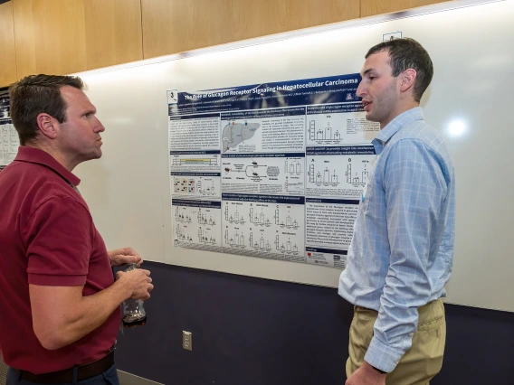 [Rheumatology’s Joshua Farr, PhD, speaks with Thadeus Carolyn, a student who works with Endocrinology’s Jennifer Stern, PhD, about a research poster on, “The role of glucagon receptor signaling in hepatocellular carcinoma.”]