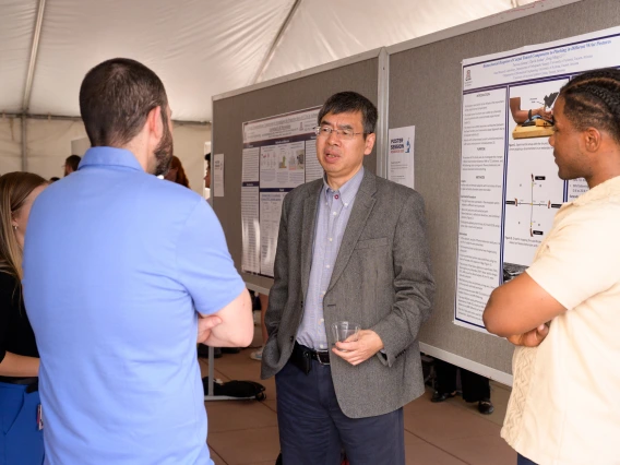 [Zong-Ming Li, PhD, the William and Sylvia Rubin Chair of Orthopedic Research at COM-T and associate director of the Arizona Arthritis Center, led by the DOM's C. Kent Kwoh, MD, discusses a poster he assisted on about carpal tunnel syndrome with co-authors Trevour Greene (right), a research lab manager, and David Jordan, PhD, MS.]