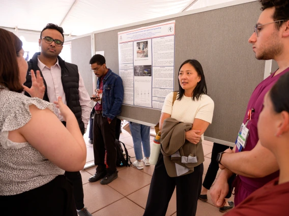 [Emergency Medicine’s Alli Min, MD, listens to a student talk about her research project at the COM-T 2025 Research Day poster session, while David Jordan, PhD (behind Dr. Min), checks his phone messages. A co-author on Jordan’s research poster, “Ultrasound shear wave speed of the transverse carpal ligament during pinching,” is the DOM Division of Rheumatology’s C. Kent Kwoh, MD, who also has been the U of A Arthritis Center director since 2013.]