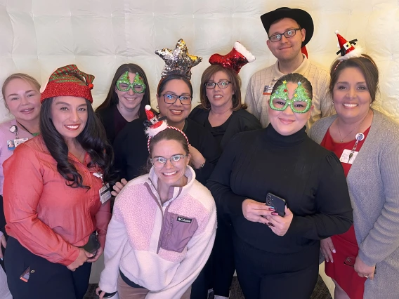 [From left, Department of Medicine clinical associate directors Monique Murillo and Monica Rodriguez, Megan Rumble, Lauren Melcher, RN, Natalie Provencia-Dean, Sylvia Lopez, RN, Xochilt Ortega, Ken Bottrill, and Gina Dominguez – sporting their photobooth headwear Dec. 3 at the 2025 DOM Year-End Faculty & Staff Luncheon.]
