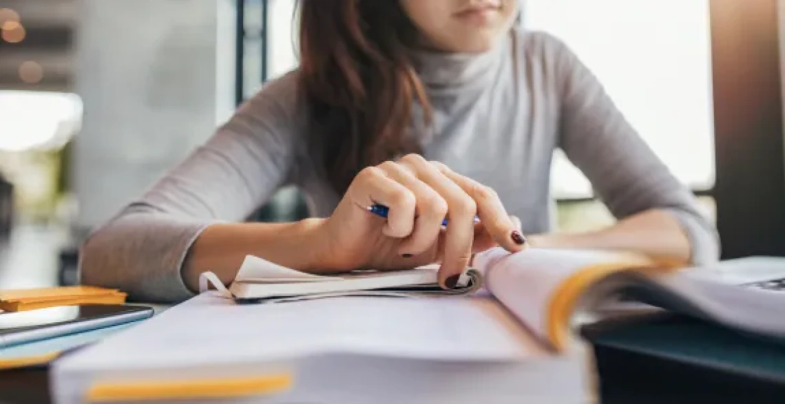 A woman at a desk, engaged in writing notes in her notebook with a pen in hand.