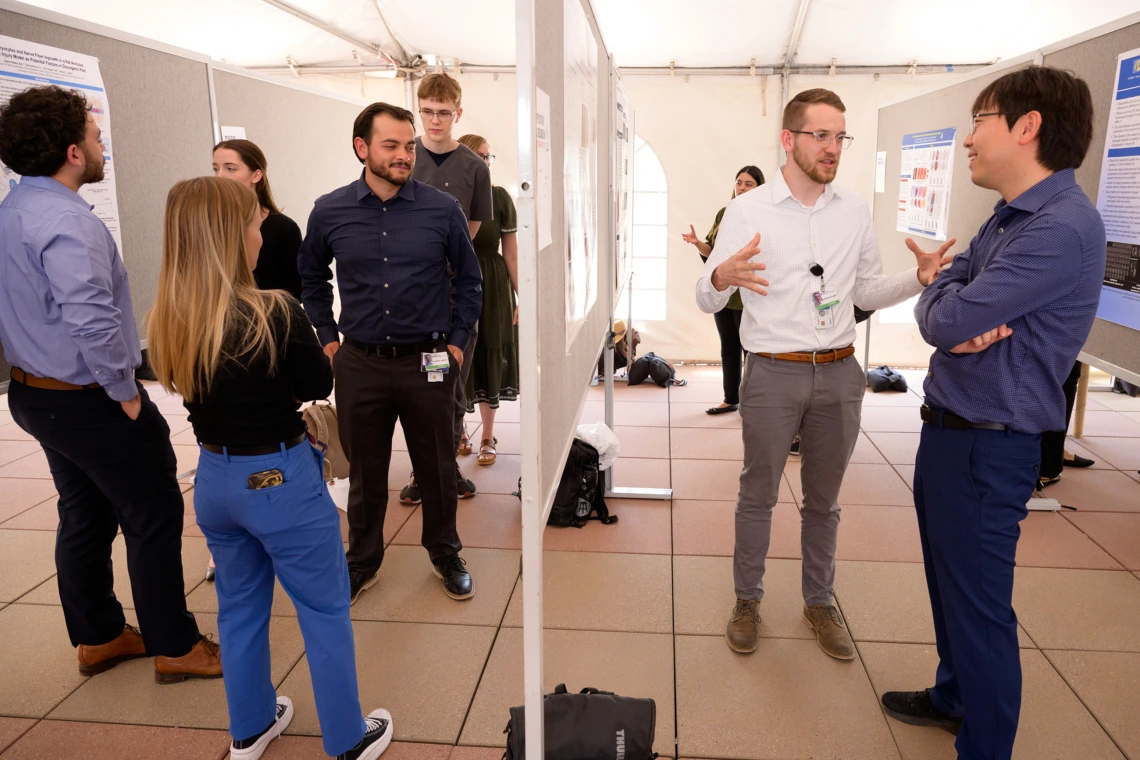 [Students, including first-year Caleb Seekins (wearing glasses on left), who’s co-president of COM-T’s Internal Medicine Student Association, chat about each other’s research posters at the COM-T 2025 Research Day poster session. Seekins’ poster is on, “Terpenes from Cannabis Sativa are Antinociceptive in a Reserpine-Induced Mouse Model of Fibromyalgia,” involving research he did working in the lab of the Department of Pharmacology’s John Streicher, PhD]