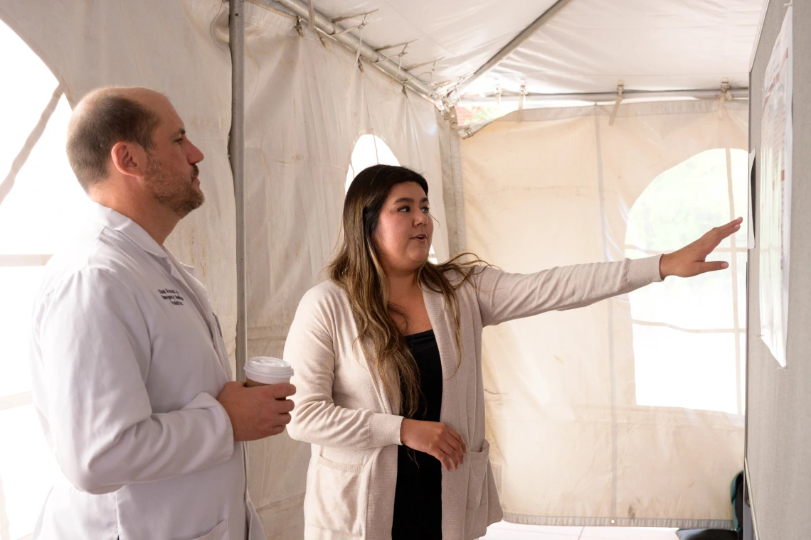 [The Department of Emergency Medicine’s Chad Viscusi, MD, listens to a student explain the research behind their poster presentation at the COM-T 2025 Research Day poster session.]